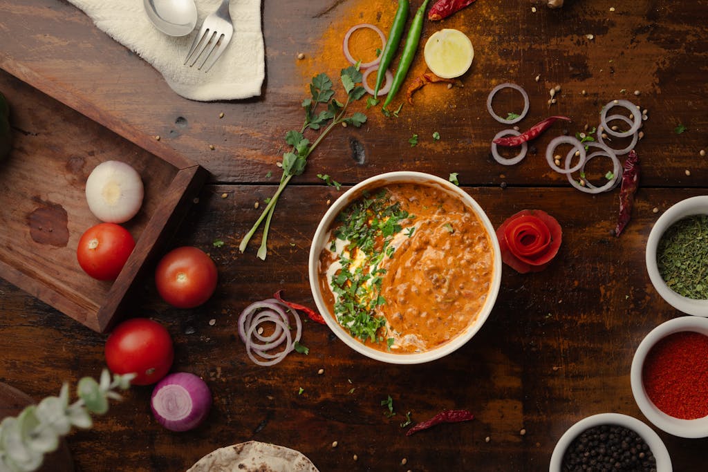 A vibrant top-down view of a flavorful Indian curry surrounded by fresh vegetables and spices.